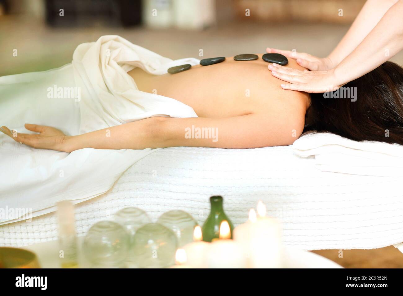 Crop Therapeut, die Massage mit heißen Steinen für unkenntlich entspannte weibliche Klientin auf dem Tisch im Spa Salon Stockfoto