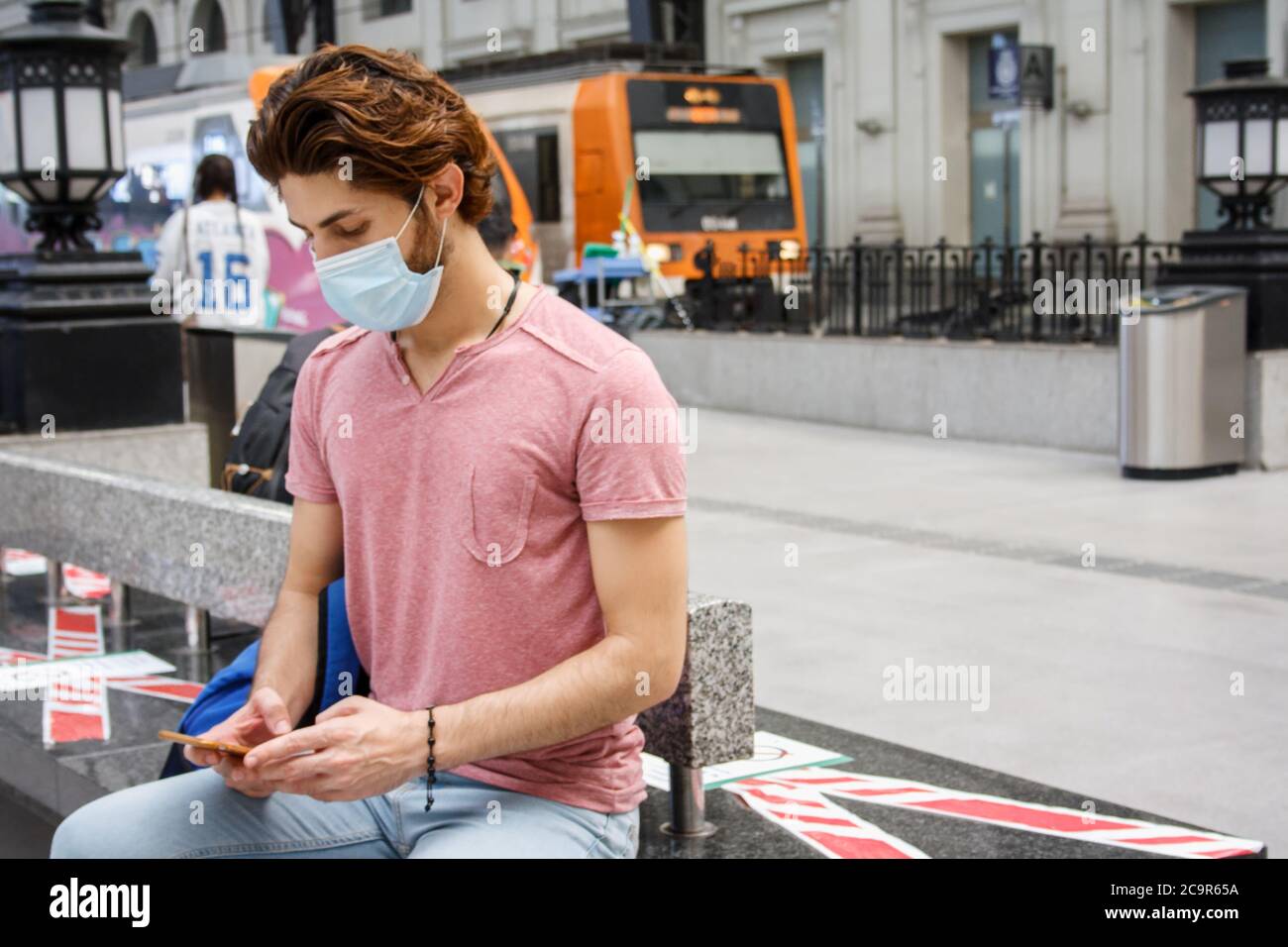 Junger Mann wartet auf dem Bahnhof. Soziale Distanzierungsmaßnahmen beibehalten. Sicher reisen. Medium kurzes Flugzeug. Horizontale Ansicht. Stockfoto