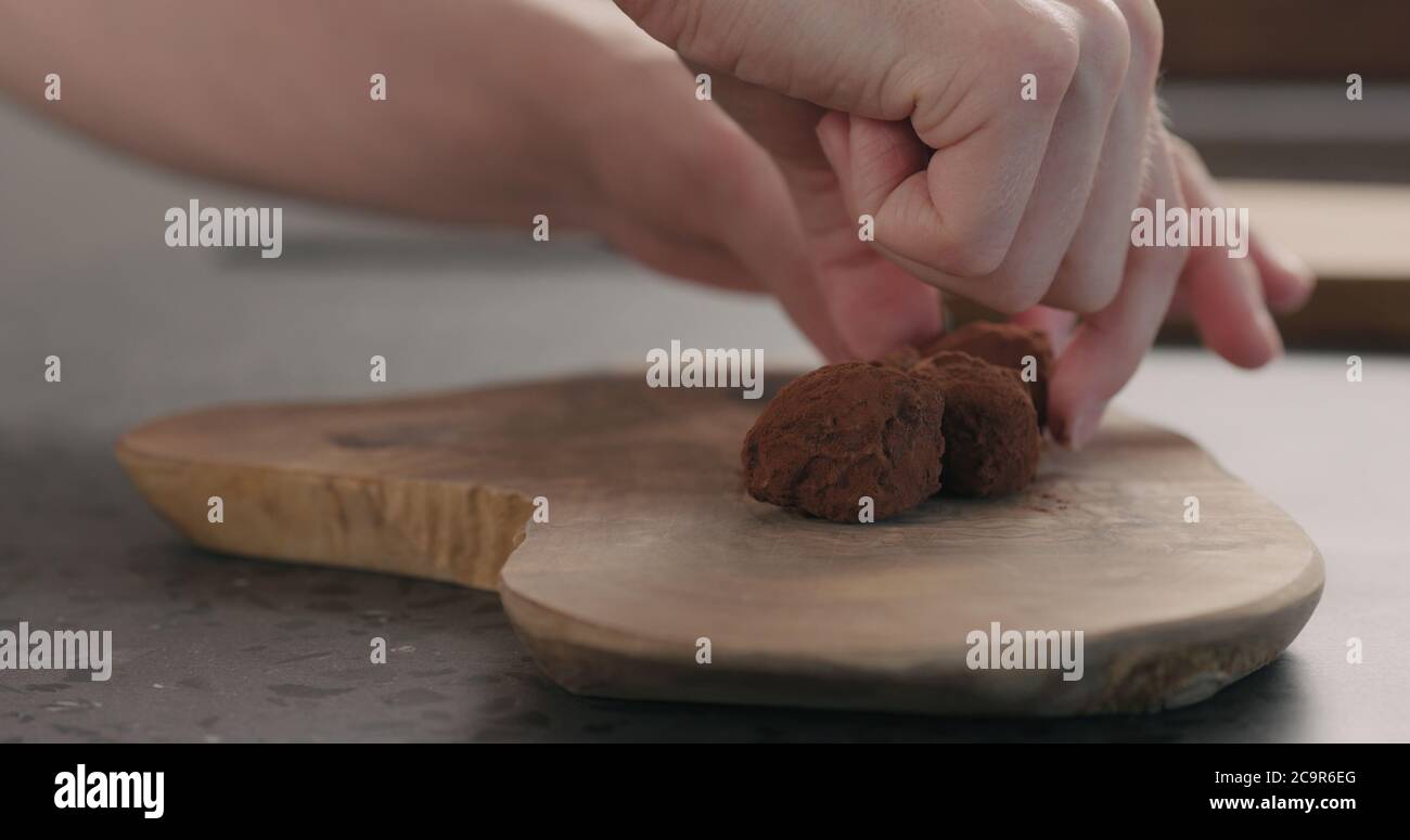 Man Hand legte handgemachte Schokoladentrüffel auf ein Holzbrett Stockfoto