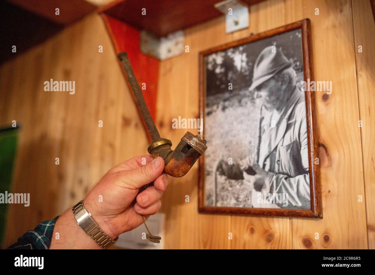 Hirte hält eine Pfeife, die früher seinem Großvater gehörte (siehe Archivfoto an der Wand), in seinem Haus im ländlichen Ungarn Stockfoto