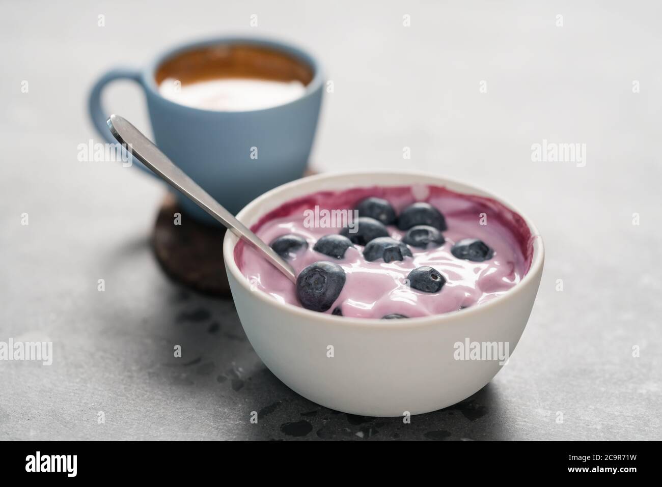 Heidelbeerjoghurt mit ganzen Beeren und einer Tasse frischen Espresso Auf konkretem Hintergrund Stockfoto