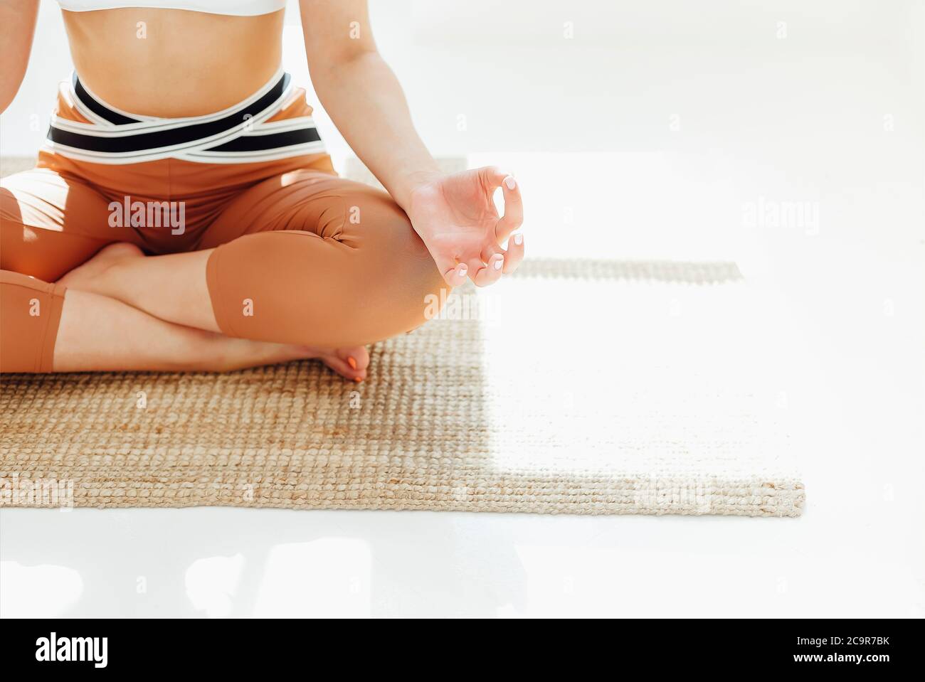 Junge Frau in Sportbekleidung sitzt mit gekreuzten Beinen und Mudra-Händen auf Matte und macht Yoga während Achtsamkeit üben Stockfoto