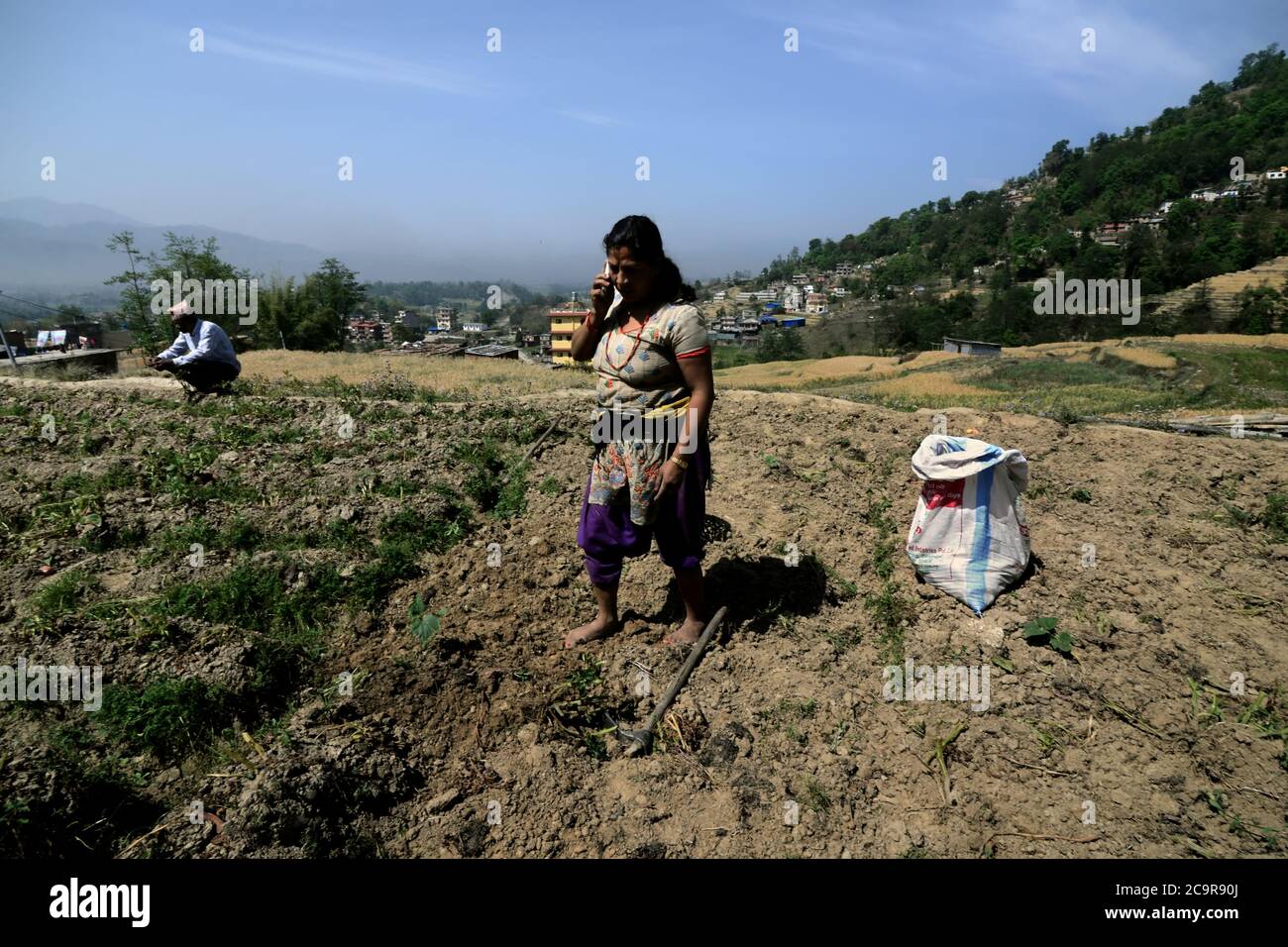 Eine Bäuerin, die eine Pause für ein Telefongespräch macht, während sie in einer ländlichen Gegend am Stadtrand von Bhaktapur, Nepal, Kartoffeln erntet. Stockfoto