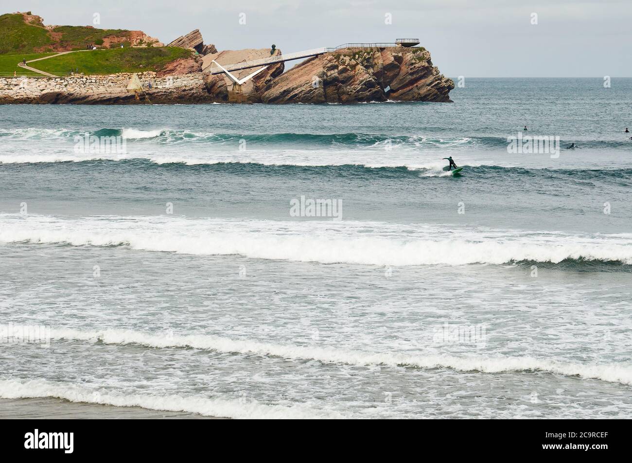 Wellenreiten am Strand Playa de Salinas mit der Halbinsel La Peñona im Hintergrund (Castrillón, Asturien, Kantabrische See, Spanien) Stockfoto