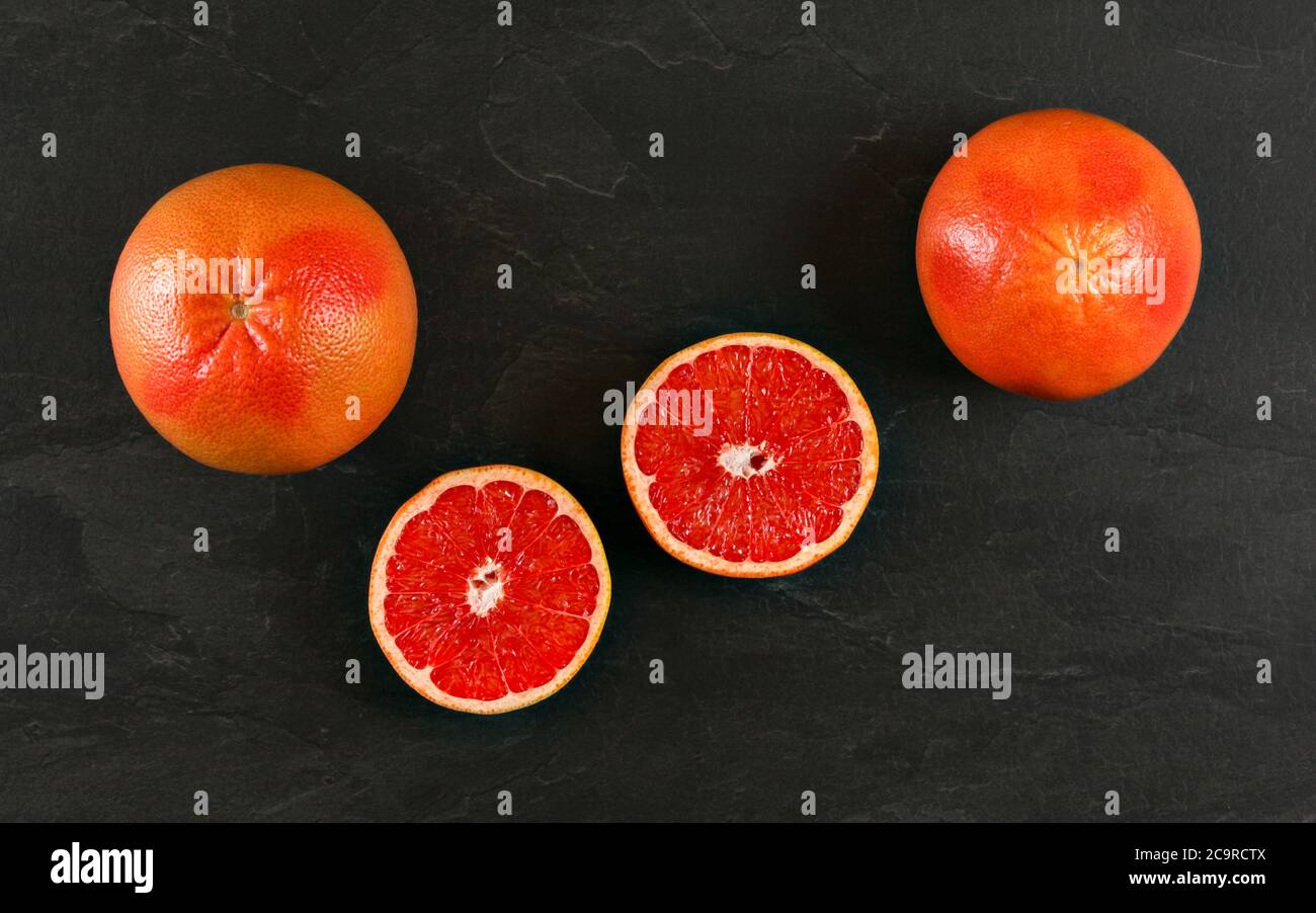 Rosa Grapefruits, eine Hälfte auf schwarzem Schiefertafel geschnitten, Draufsicht. Stockfoto