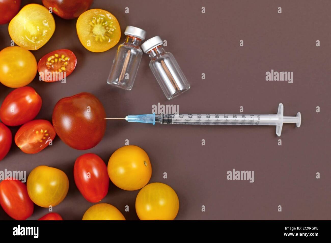 Konzept für gentechnisch veränderte Lebensmittel mit Tomaten, Injektionsspritze und leeren medizinischen Fläschchen auf dunkelbraunem Hintergrund Stockfoto