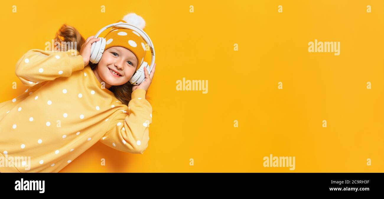 Fröhliche niedliche kleine Mädchen in guter Stimmung hören moderne Technologie Kopfhörer auf einem gelben Hintergrund. Kopierbereich für Banner in der Draufsicht. Stockfoto