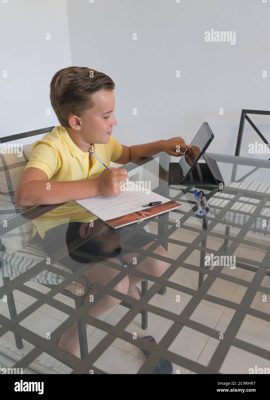 Junge im Gespräch mit Klassenkamerad während Videoanruf auf Tablet und diskutieren Hausaufgaben, während am Tisch in modernen hellen Raum sitzen. Stockfoto