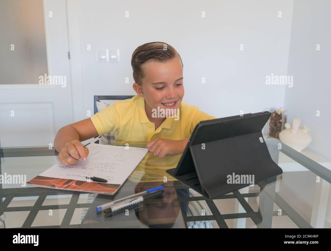 Junge im Gespräch mit Klassenkamerad während Videoanruf auf Tablet und diskutieren Hausaufgaben, während am Tisch in modernen hellen Raum sitzen. Stockfoto