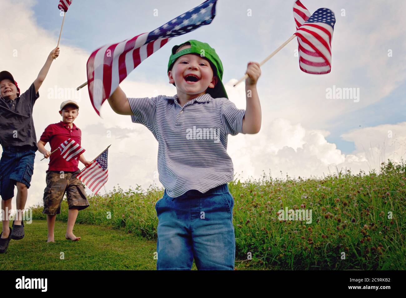 Drei Jungen halten American Flags begeistert, während sie winken und Der jüngste Junge vorne ist der glücklichste von allen Mit dem größten Lächeln Stockfoto