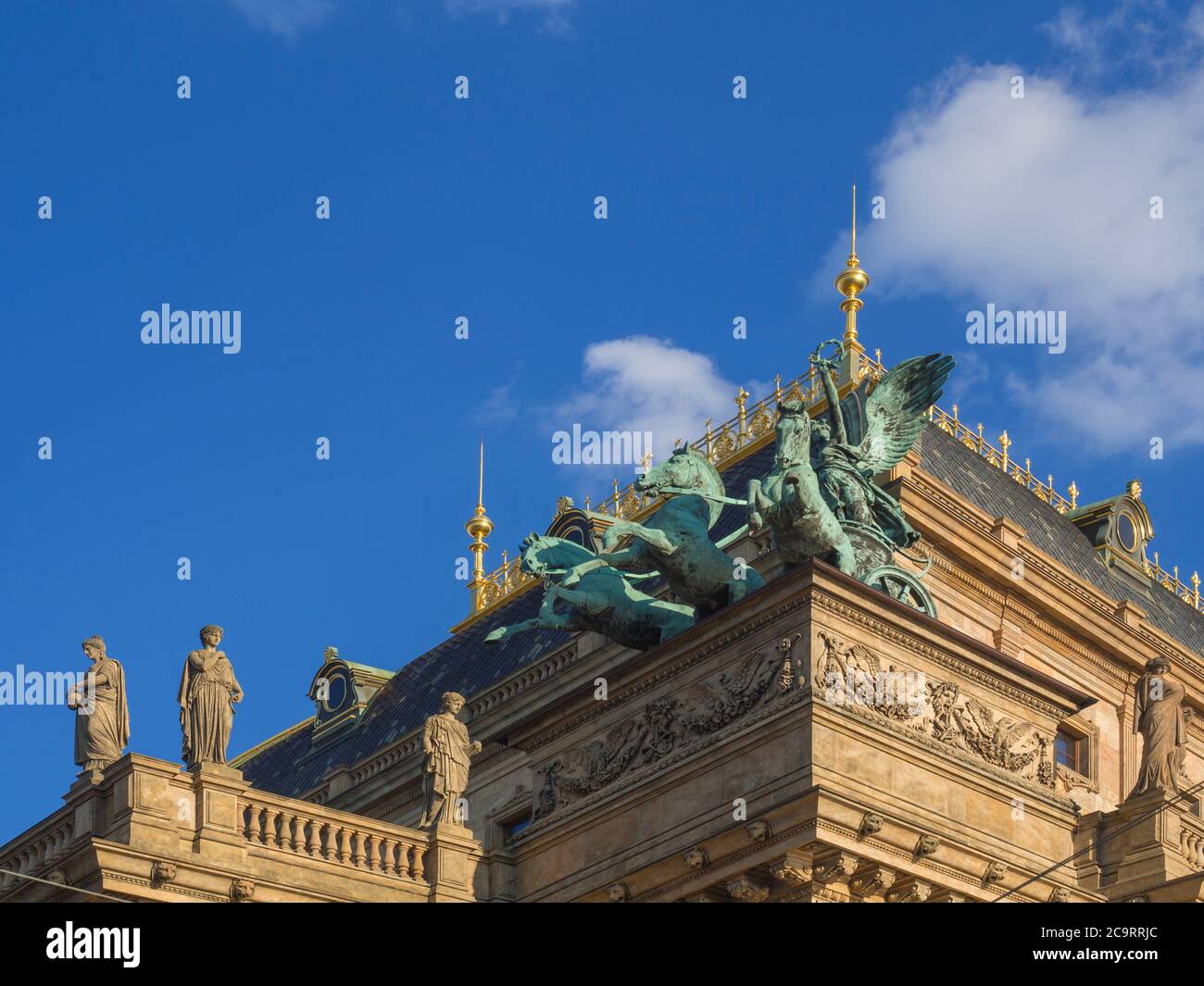 Verzierte Ecke Detail Prager Nationaltheater Gebäude mit Bronze drei Pferd Wagen auf dem Dach und Stein weibliche Statuen, blauen Himmel weißen Wolken b Stockfoto