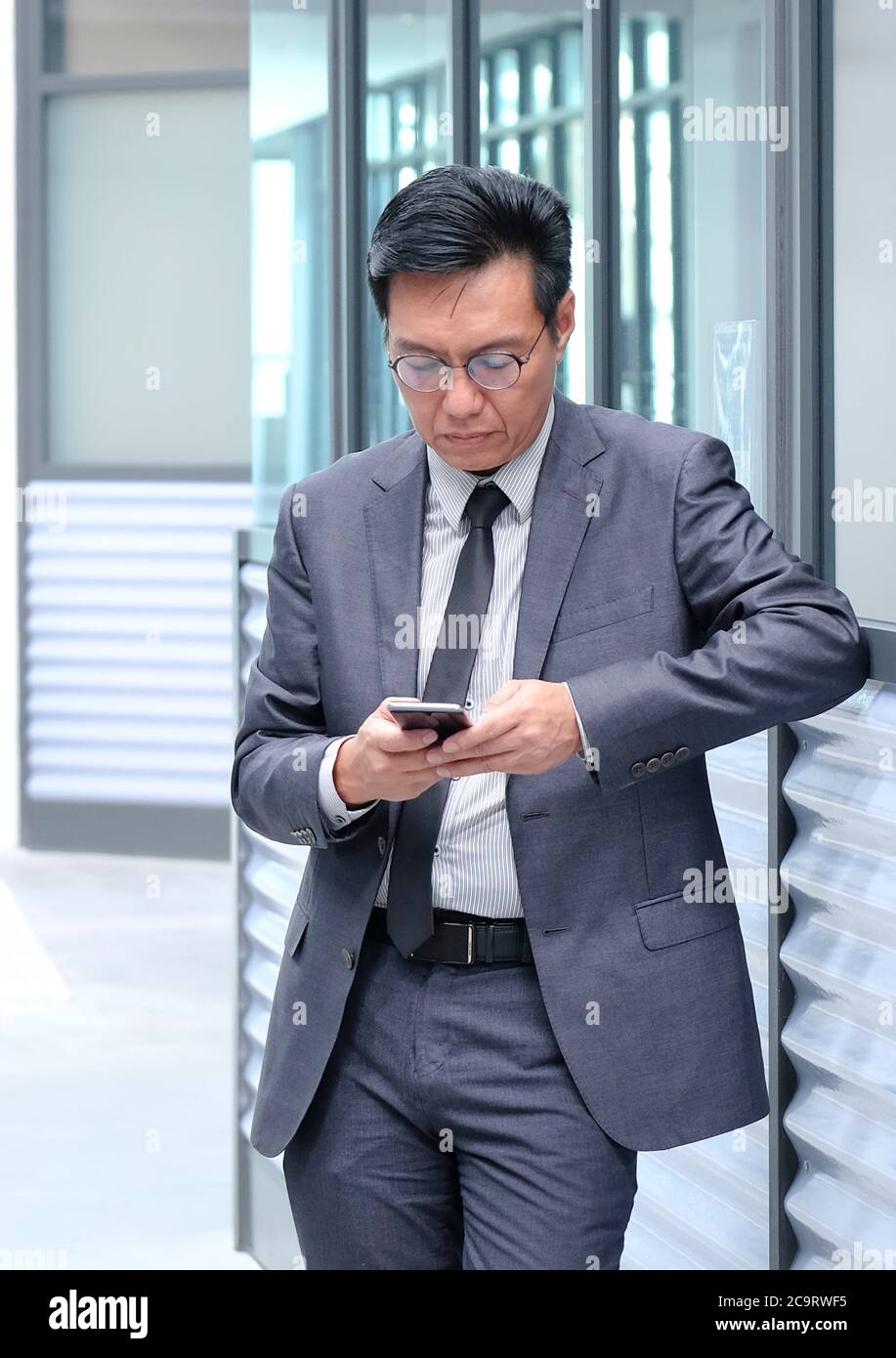 Chinesischer Geschäftsmann in Anzug und Krawatte, mit seinem Handy. Stockfoto