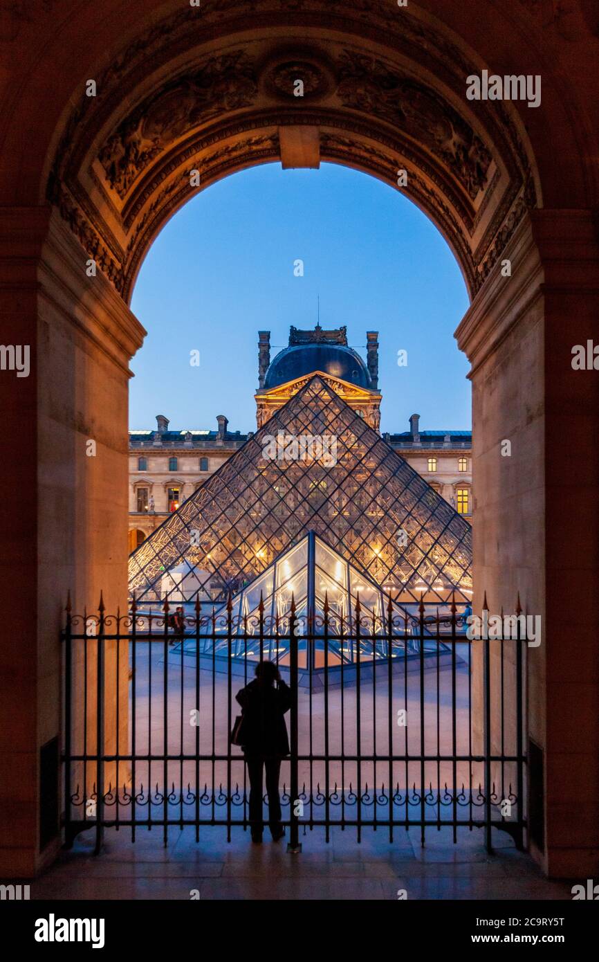 Eine Silhouette eines Touristen, der ein Bild von der beleuchteten Glaspyramide im Louvre Museum, Paris macht Stockfoto