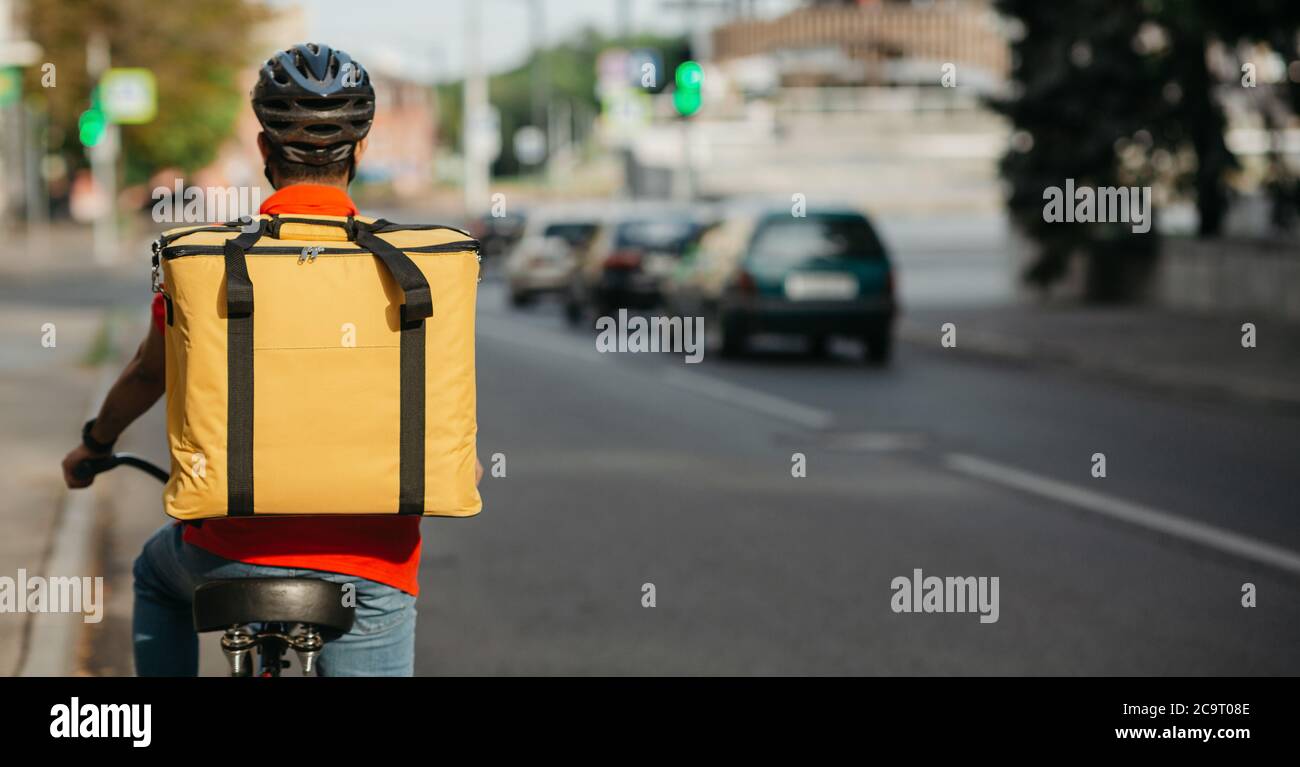 Moderne schnelle Lieferung in der Stadt. Junger Mann im Helm mit Rucksack fährt ein Fahrrad auf der Straße Stockfoto