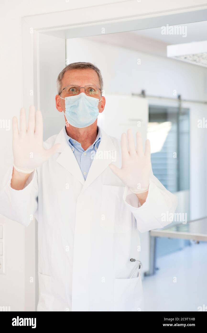 Besorgt reifer Arzt mit OP-Maske stoppen Menschen von der Eingabe in eine Operation oder ein Krankenhaus Stockfoto