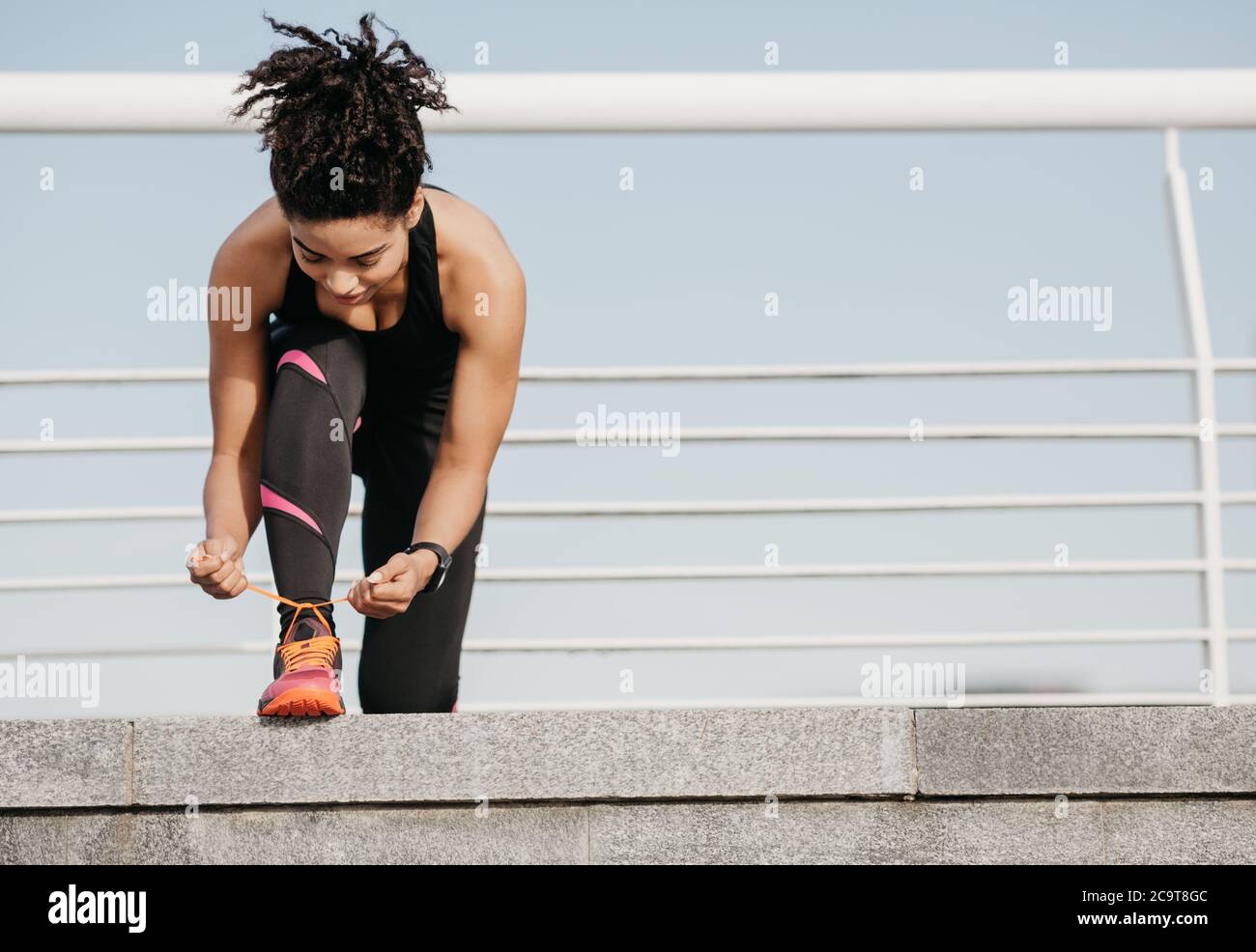 Beginn des morgendlichen Trainings. afroamerikanische junge Frau in Sportbekleidung mit Fitness-Tracker binden Schnürsenkel im Stadion Stockfoto