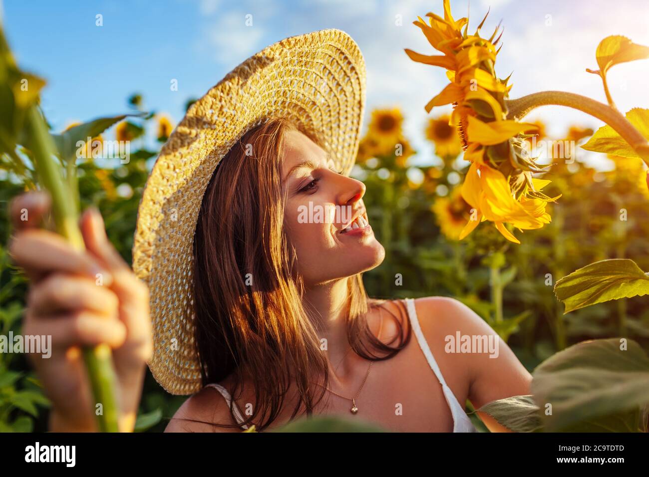 Junge glückliche Frau, die im blühenden Sonnenblumenfeld frei riechende Blumen fühlt. Sommerurlaub Stockfoto Junge glückliche Frau, die im blühenden Sonnenblumenfeld frei riechende Blumen fühlt. Sommerurlaub Stockfoto