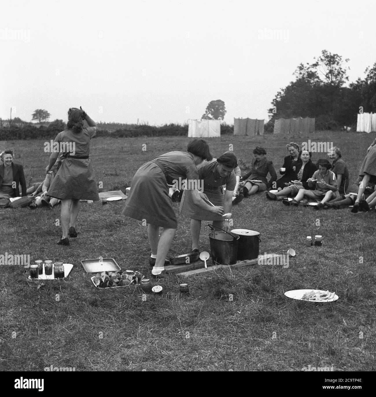 1950s, historisch, Mädchen Führer im Lager, mit Besuchern, möglicherweise Familienmitglieder, mit zwei Führungen servieren Tassen possiby Suppe aus großen Stahlschalen, mit Scheiben von Brot, Kuchen und Marmelade auf dem Gras, England, Großbritannien. Stockfoto