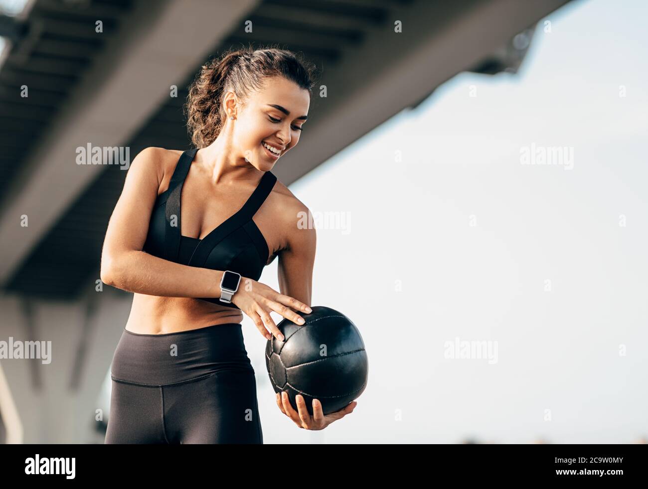 Lächelnde Frau in Sportswear Ausübung mit Medizin Ball unter einem autobahn Stockfoto