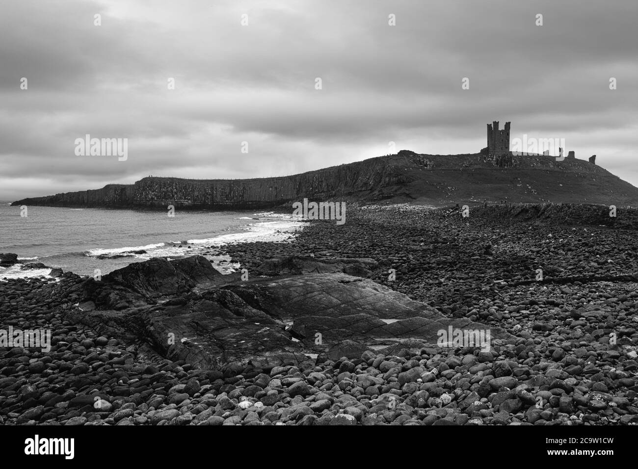 Die Ruinen von Dunstanburgh Castle, Northumberland, England, UK von Embleton Bay an einem bewölkten, düsteren Tag. Schwarz-Weiß-Version Stockfoto