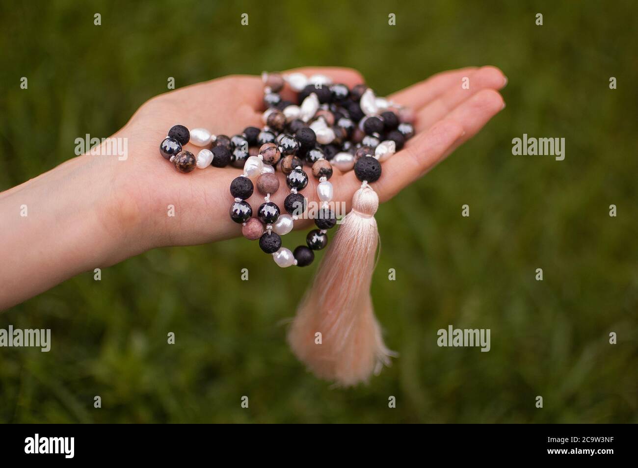 Weibliche Hand hält ein buddhistisches Japa mala aus 108 Natursteinen Perlen für Meditation auf grünem Gras Hintergrund Stockfoto