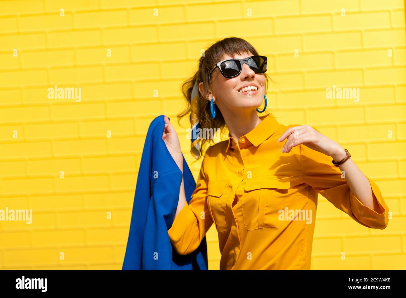 Fröhliches Mädchen vor dem Hintergrund einer hellgelben Wand in einem gelben Hemd mit einer abgebildeten Jacke. Lächelnd und glücklich. Stockfoto