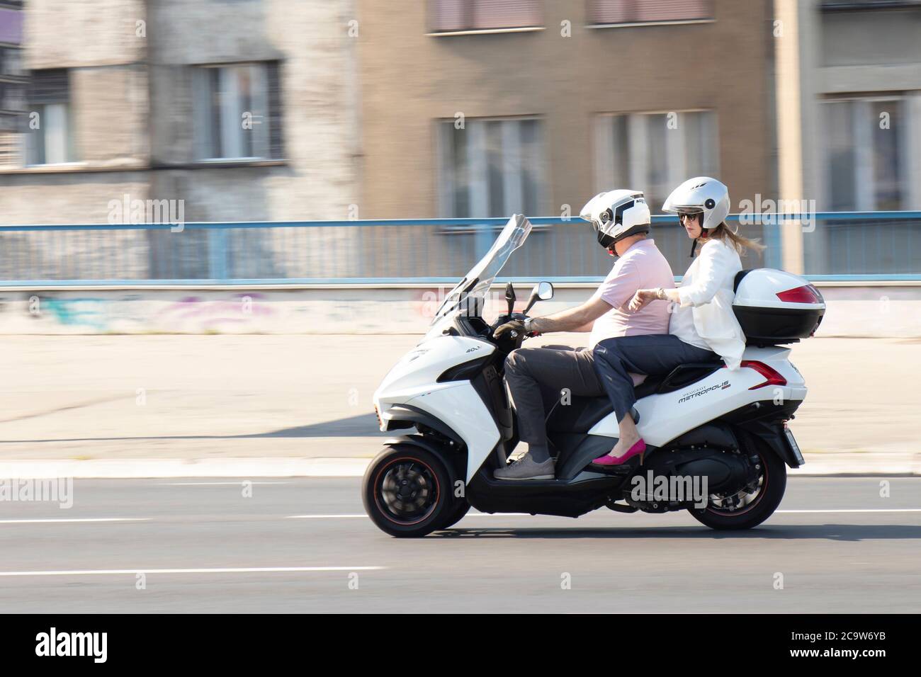 Belgrad, Serbien - 31. Juli 2020: Reifes Paar, das auf einem dreirädrigen Motorrad auf der Stadtstraße fährt, und eine Frau überprüft die Zeit an ihrer Armbanduhr Stockfoto