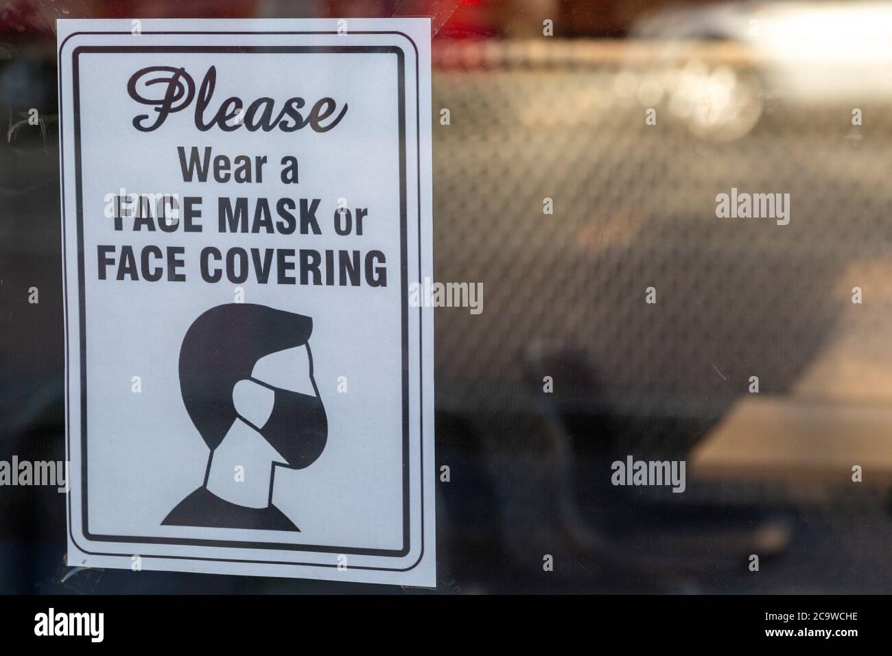 Ein Schild in einem Schaufenster, das besagt, dass Sie müssen Tragen Sie Gesichtsmasken oder Gesichtsbedeckungen in Übereinstimmung mit der Regierung Richtlinien während des Coronavirus-Ausbruchs Stockfoto