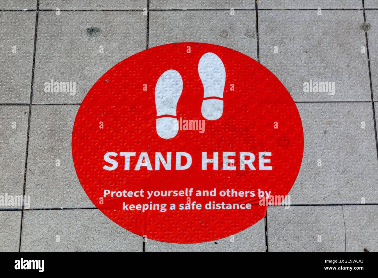 Ein Schild auf dem Boden vor einem Geschäft, auf dem Kunden mitgeteilt wird, wo sie Schlange stehen sollen, damit sie sich gemäß den Richtlinien der Regierung sozial distanzieren Stockfoto