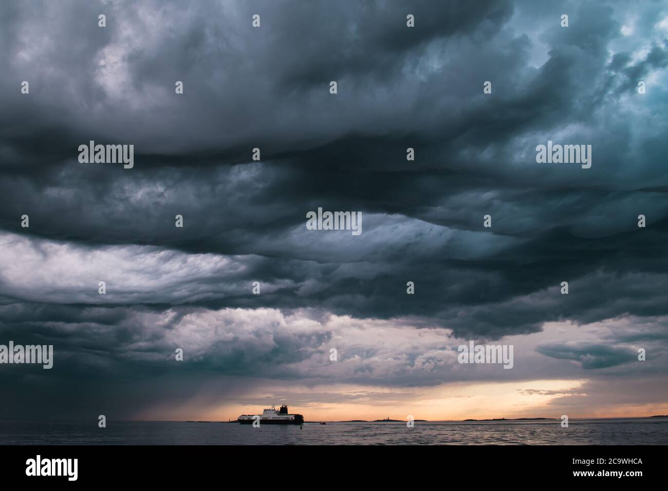 Ein Frachtschiff unter stürmischen Wolken bei Sonnenuntergang im südlichen Schären von Göteborg, Schweden Stockfoto