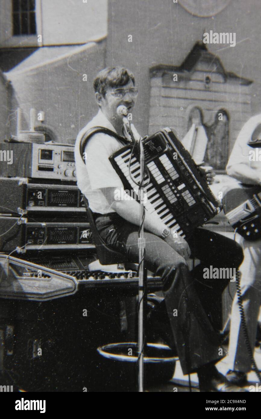 Feine 70er Jahre Vintage schwarz-weiß Lifestyle-Fotografie eines Akkordeonspielers bei einem Straßenfest im Freien. Stockfoto