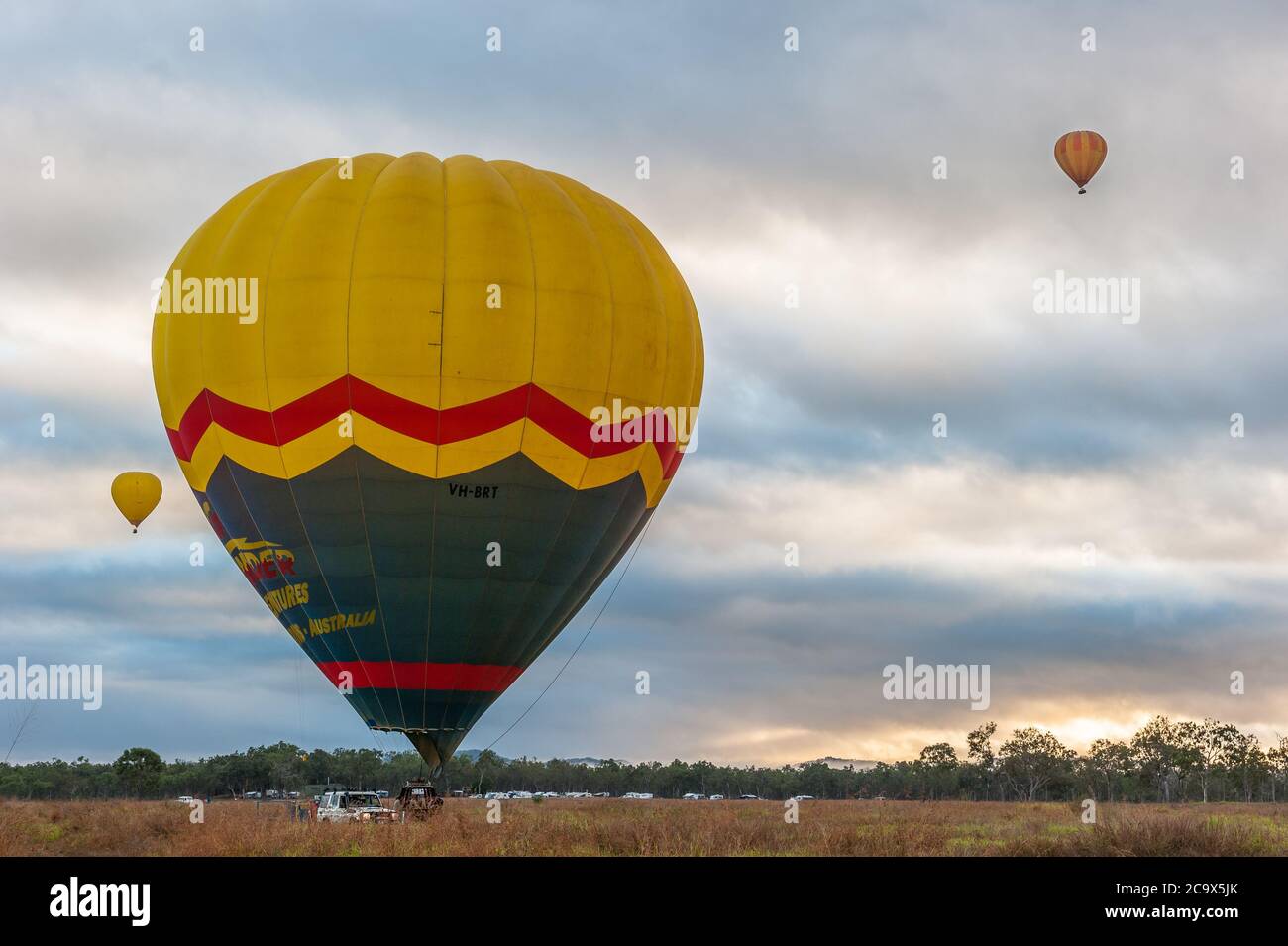Als die Sonne aufgeht, starten drei bunte Ballons mit touristisch gefüllten Körben zu einem Flug über Mareeba in Queensland, Australien. Stockfoto