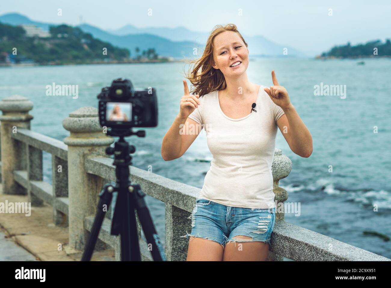 Eine junge Bloggerin führt ihren Videoblog vor einer Kamera am Meer. Blogger-Konzept Stockfoto