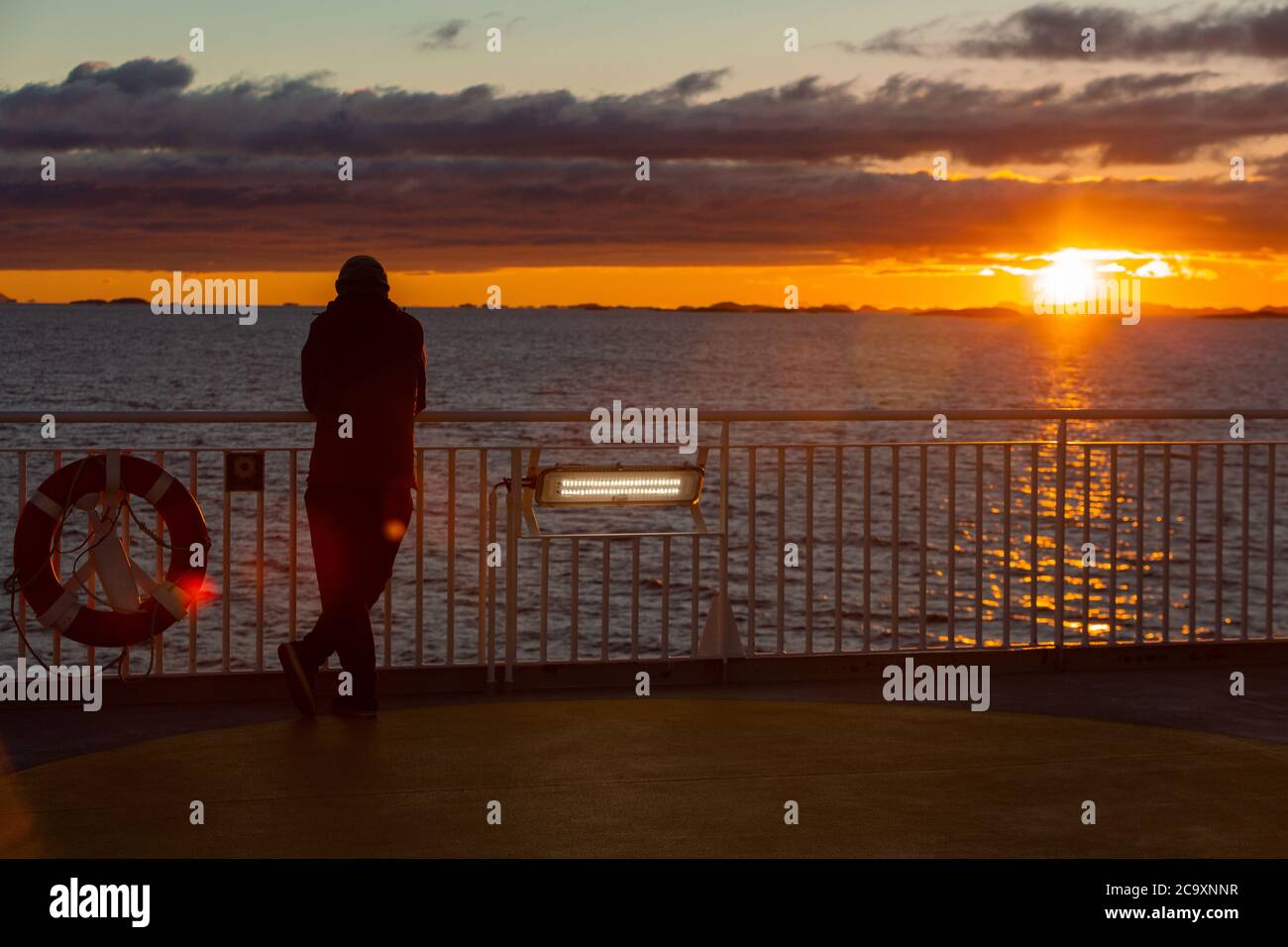 Ein Mann steht auf dem Deck der Fähre und beobachtet den Sonnenuntergang am Atlantischen Ozean. Polarsonne Stockfoto