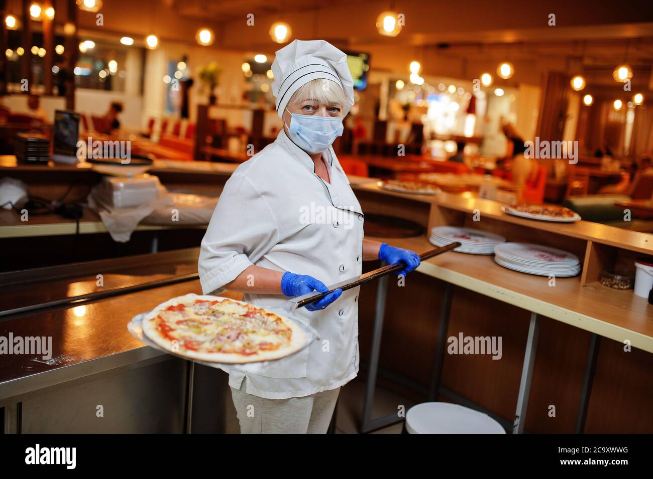 Pizzahersteller in Schutzmaske in der Pizzeria arbeiten. Stockfoto