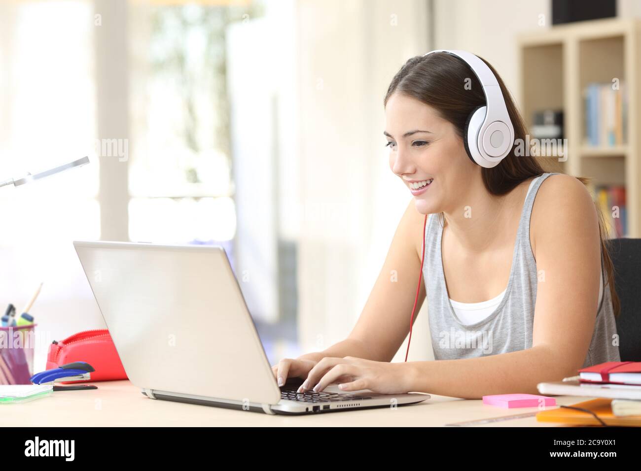 Fröhliche Studentin elearning auf Laptop mit Kopfhörern sitzen auf einem Schreibtisch zu Hause Stockfoto