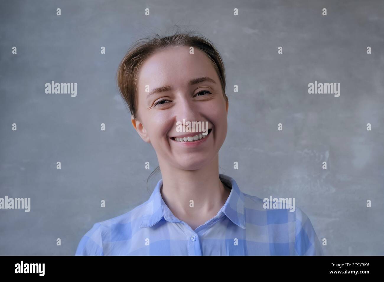 Porträt von jungen positiven Hipster, Student oder Unternehmerin Frau in blau kariert Hemd lächelnd und Blick auf die Kamera in Raum mit grauen Wand. Personen und Stockfoto