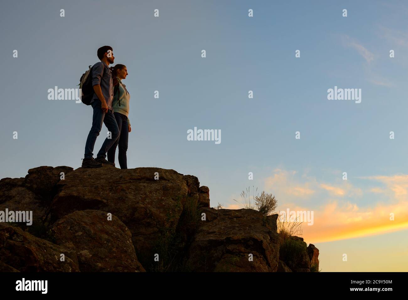 Ein paar junge Reisende, die bei Sonnenuntergang auf der Spitze des Felsens stehen. Familienreisen und Abenteuer Konzept Stockfoto