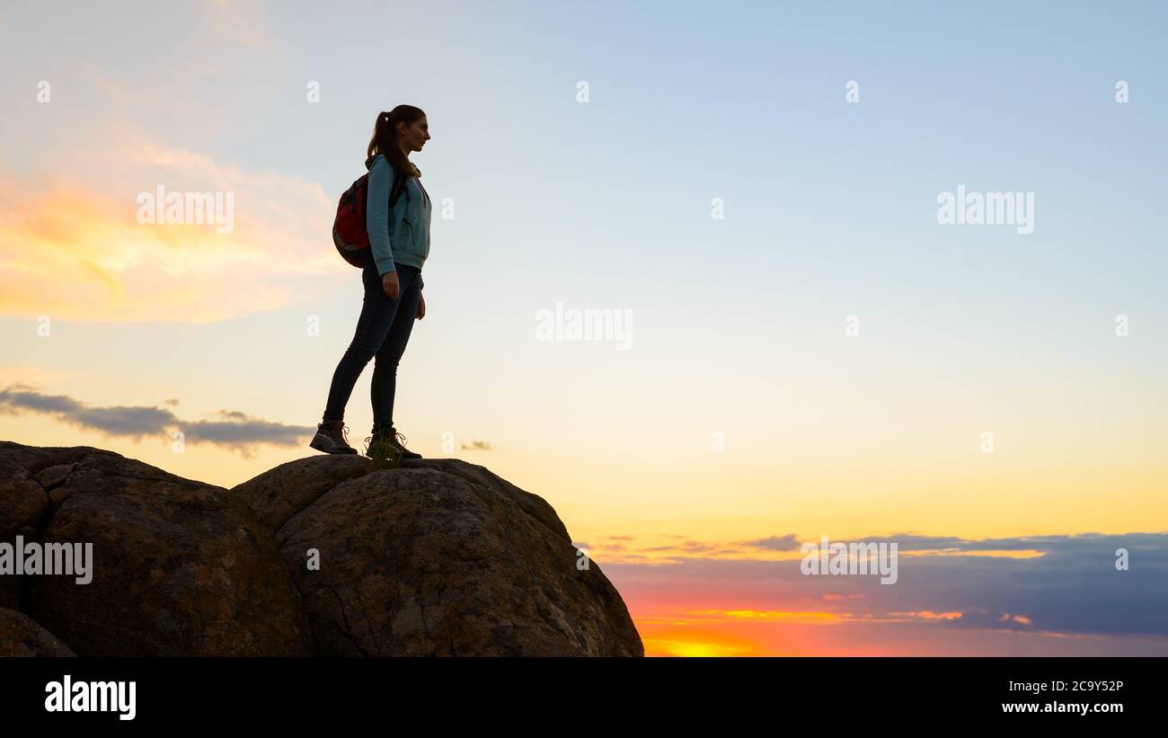 Junge Frau Reisende mit Rucksack stehend auf der Oberseite des Felsens bei Sommer Sonnenuntergang. Reise- und Abenteuerkonzept. Stockfoto