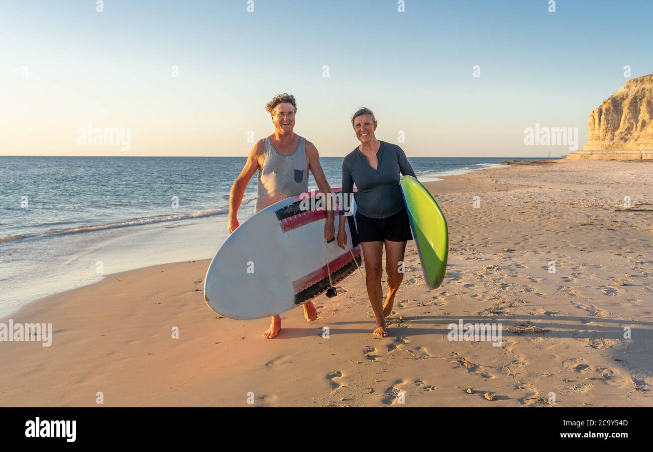 Reifes Paar mit Surfbrettern am schönen Strand, das Paradies und aktiven Lebensstil genießen. Attraktiv fit Mann und Frau Surfen und Spaß haben. In Trave Stockfoto