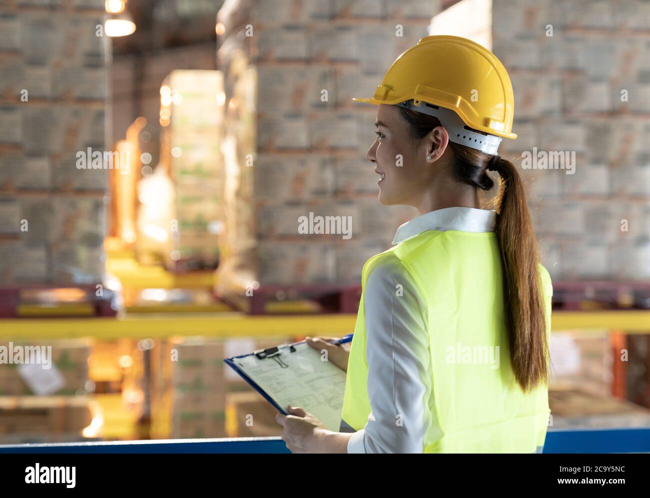 Seitenansicht der asiatischen Lagerarbeiterin mit einem Flipchart-Diagramm mit Lagerhaus im Hintergrund. Wiedereröffnung von Business Ware Stockfoto