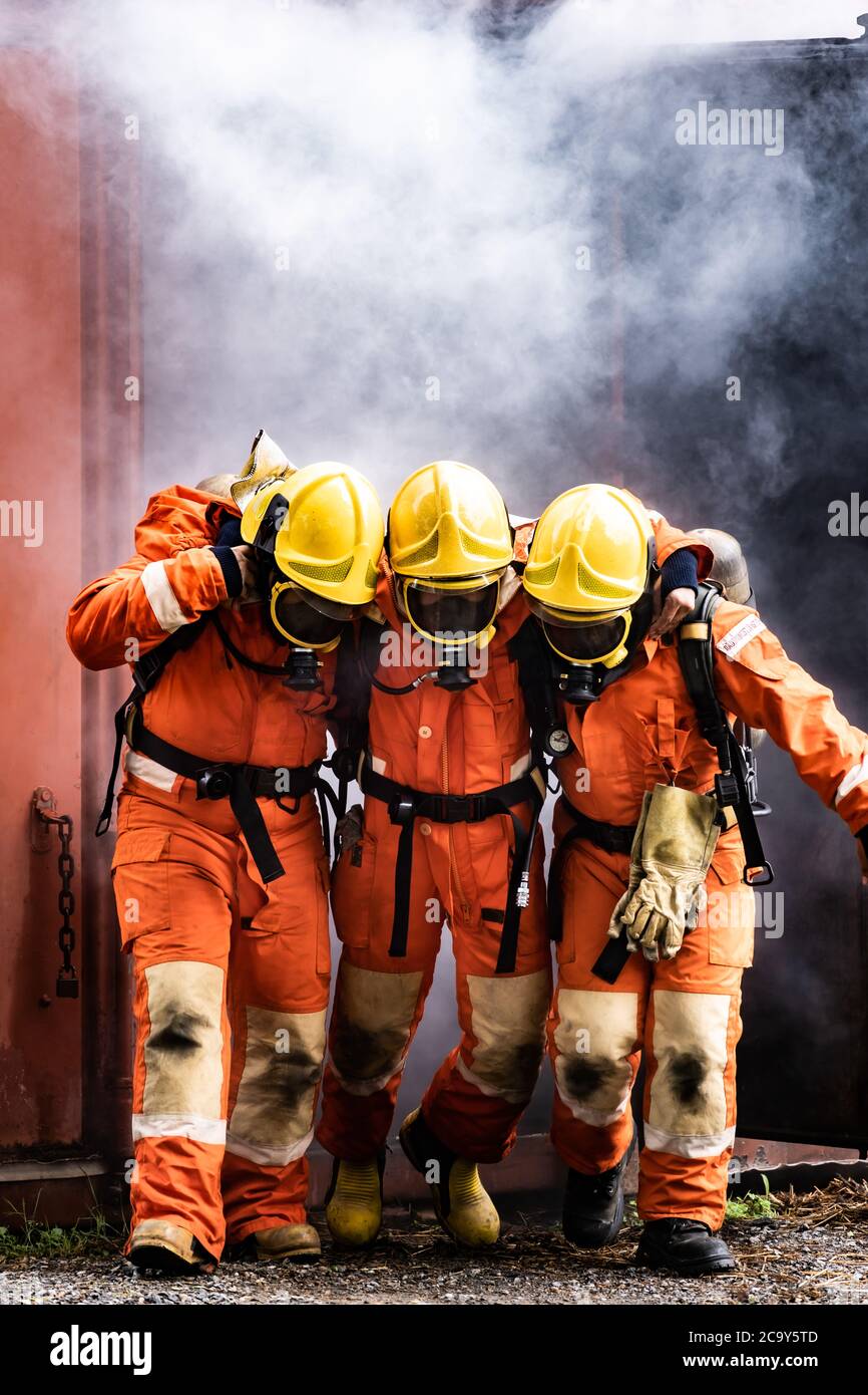 Asiatische Feuerwehrleute retten ihren Teamkollegen vor brennenden Gebäuden. Feuerwehrmann Sicherheitsrettung vor Unfall und öffentlichen Dienst Konzept. Stockfoto