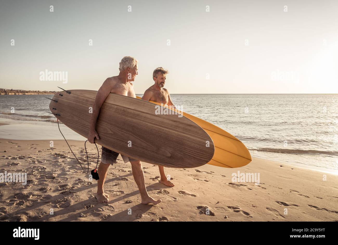 Zwei reife Männer, die mit Surfbrettern am wunderschönen Strand spazieren und das Paradies und den Lebensstil im Ruhestand genießen. Attraktiv fit ältere Erwachsene Freunde Spaß haben Stockfoto
