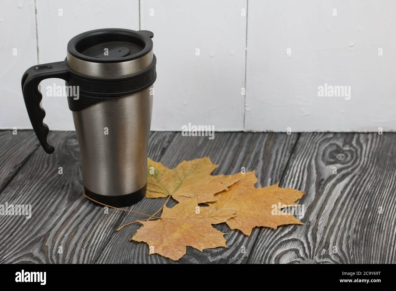 Thermo Becher auf einer Pine Board Oberfläche. In der Nähe sind getrocknete Ahornblätter. Stockfoto