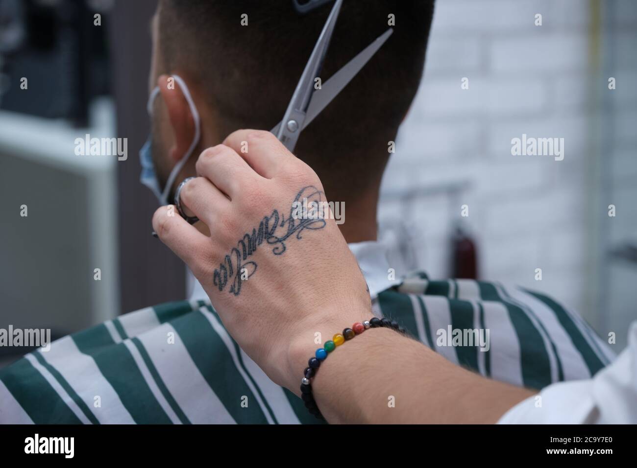 Friseurhands mit Tattoos und Armbänder Schneiden von Haaren mit Schere und  Vintage Kamm mit Schutzmaske, horizontales Format Stockfotografie - Alamy