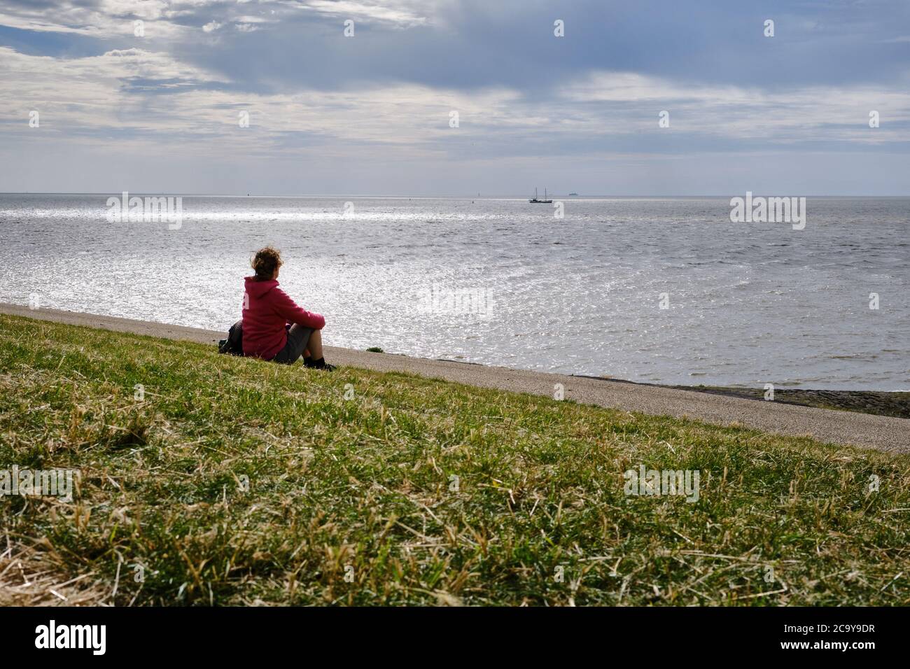 Harlingen,Niederlande,Juli,23,2020:Silhouette Rückseite der jungen Frau auf einem Deich mit Blick auf das Wattenmeer. Denken an Probleme während der Corona-Krise Stockfoto