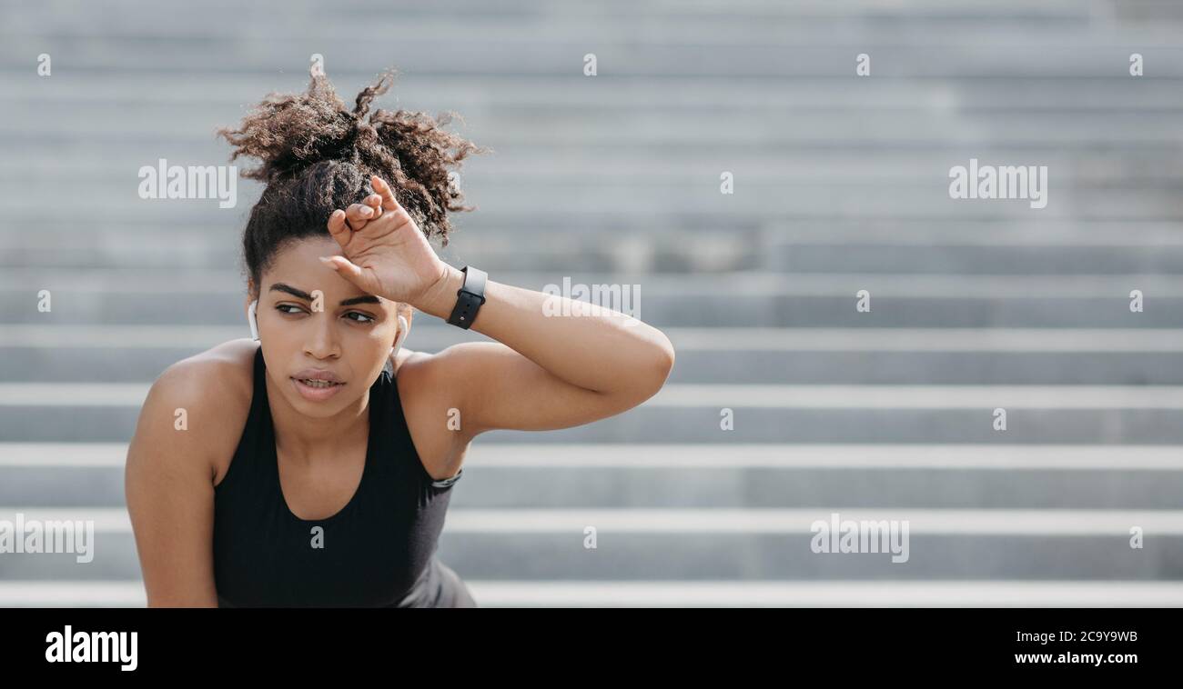 Hartes Training und Ruhe. Müde Frau mit Kopfhörer und Fitness-Tracker wischt Schweiß von der Stirn Stockfoto