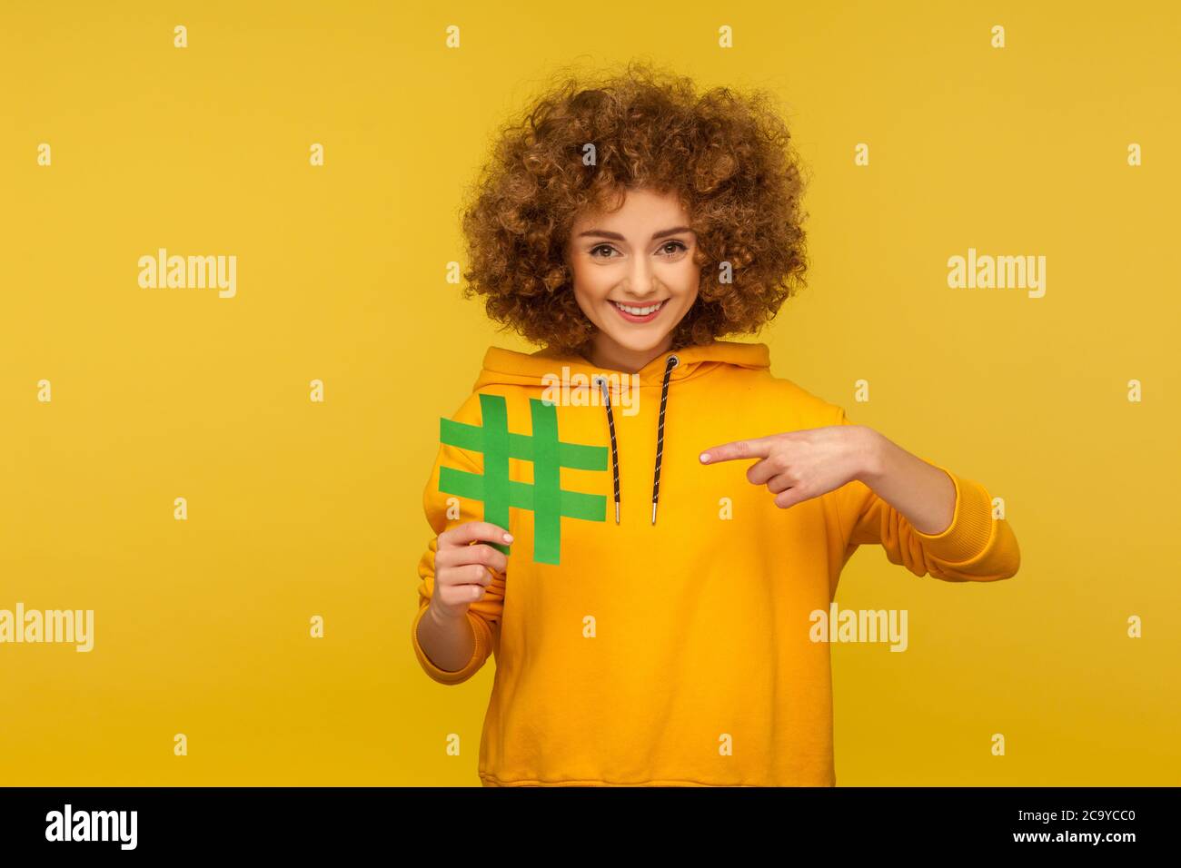 Internet-Trends. Porträt einer fröhlichen lockigen Frau im urbanen Stil Hoodie zeigt auf große Hashtag-Zeichen, was Blog-Empfehlung, Tagging Vira Stockfoto