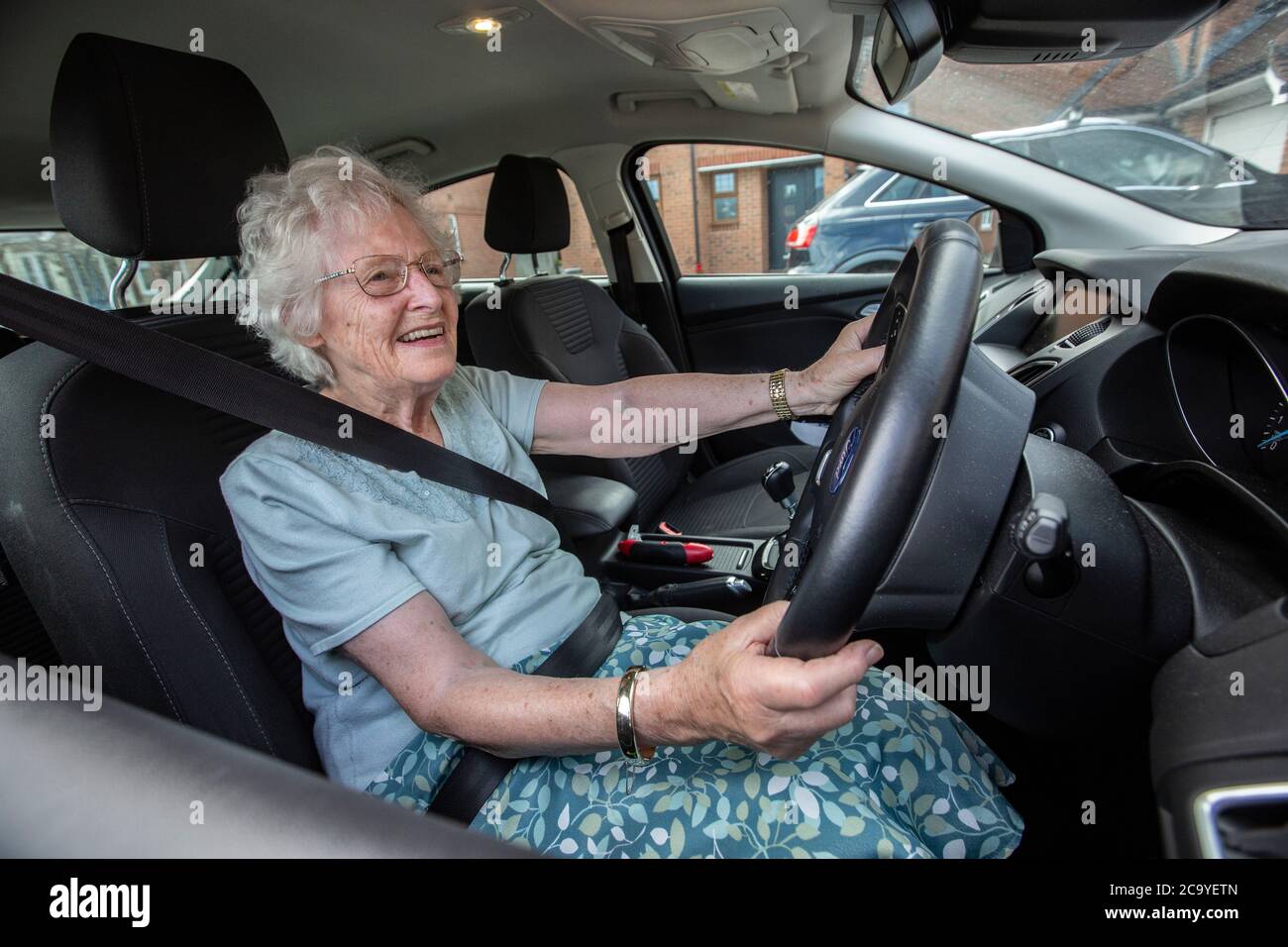 Ältere Frau in den 80ern saß auf dem Fahrersitz ihres Autos, England, Vereinigtes Königreich Stockfoto