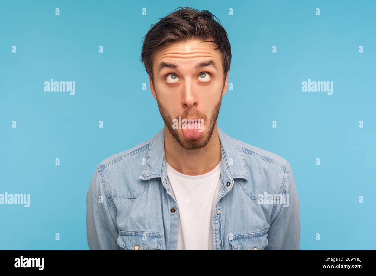 Porträt des Idiot Mann in Denim-Shirt machen dumm humorvollen Gesicht mit gekreuzten Augen und Zunge aus, zeigt komisch dumm hirnlosen Gesichtsausdruck. i Stockfoto